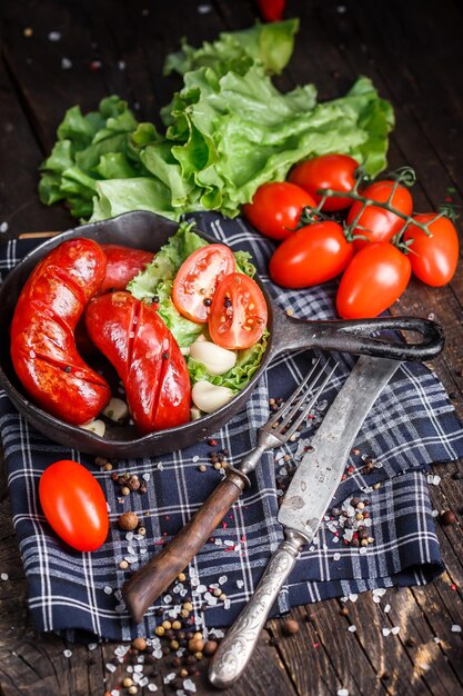 Foto cibo casereccio, salsiccia grande fritta in padella, pomodorini e lattuga scura e lunatica