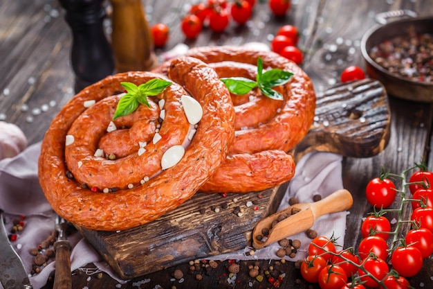Homemade food, smoked sausage rounded with spices and cherry tomatoes, on a kitchen cutting board,