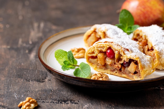 Homemade fragrant strudel with apples and cinnamon on a plate on a wooden background with space for text