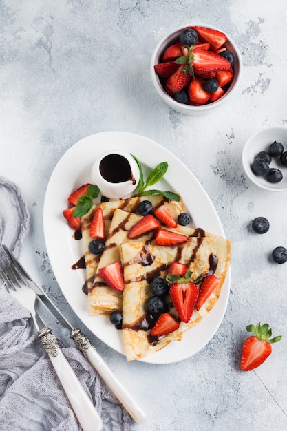 Frittelle di crepe suzette francesi fatte in casa con salsa di cioccolato, fragole fresche e miele per colazione in piatto di ceramica bianca spazio per testo o ricetta. vista dall'alto.