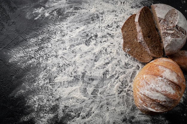 Homemade fresh baked bread with flour on a dark stone background. Top view. Empty space for text. Flatlay