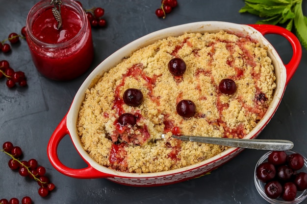 Homemade fresh cherry crumble pie with whole wheat flour in ceramic form on a dark background