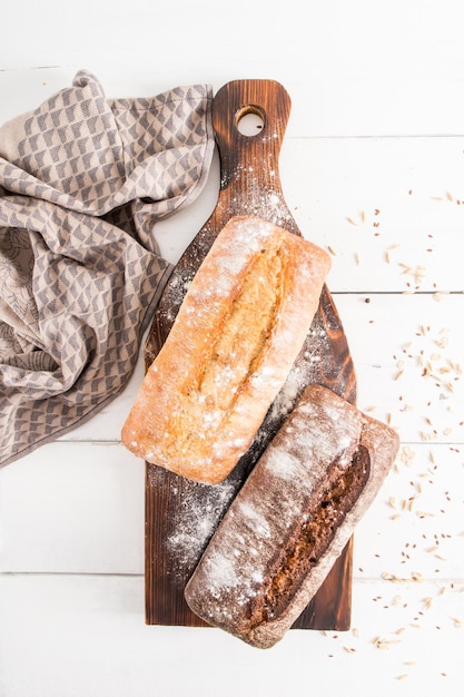 Homemade freshly baked chebatta of two types of flour on a\
wooden kitchen board and a white wooden table vertical top\
view