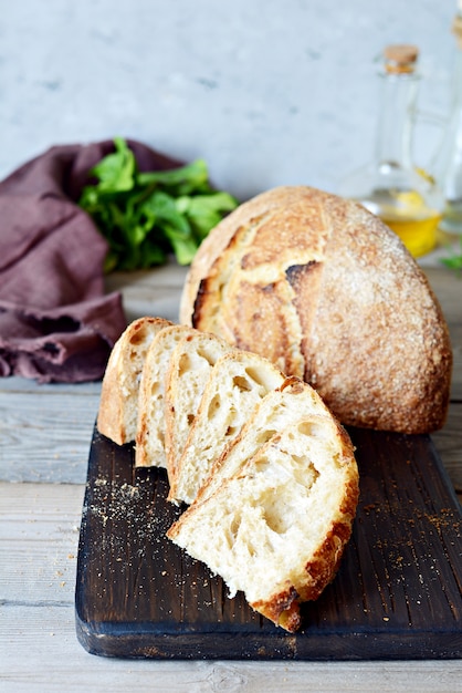 Homemade Freshly Baked Country Bread  made from wheat and whole grain flour on a gray-blue background. French Freshly baked bread. Slicing homemade bread into slices on a wooden board