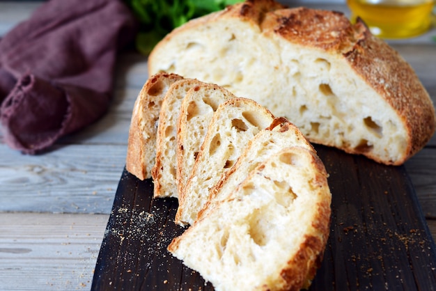 Homemade Freshly Baked Country Bread  made from wheat and whole grain flour on a gray-blue background. French Freshly baked bread. Slicing homemade bread into slices on a wooden board