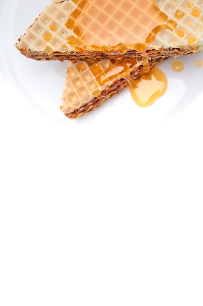 Homemade freshly baked waffle cake on a white plate topped with honey on an isolated white background