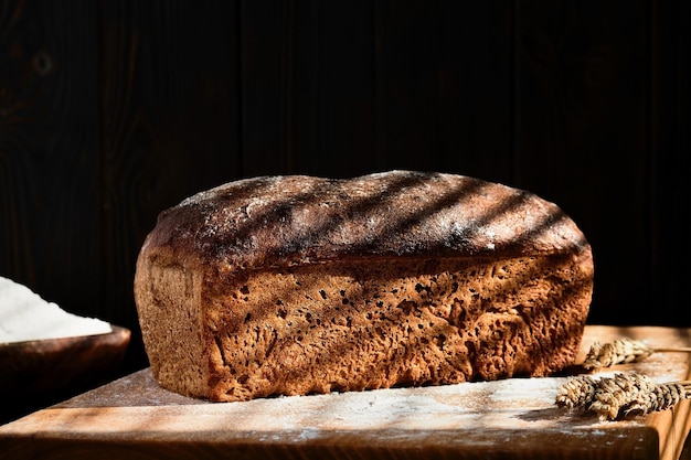 Homemade freshly baked whole grain bread made from rye and\
wheat sourdough selective focus on a loaf of bread dark mood\
traditional techniques loave innovating bread slow carb baking