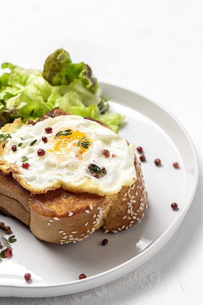 Homemade fried eggs with brioche and lettuce salad on white plate