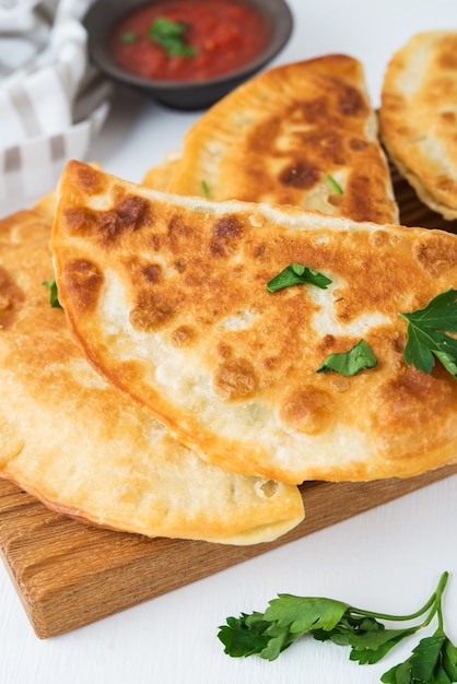 Homemade fried empanadas with pork, chebureks with mushrooms on a wooden board, close up