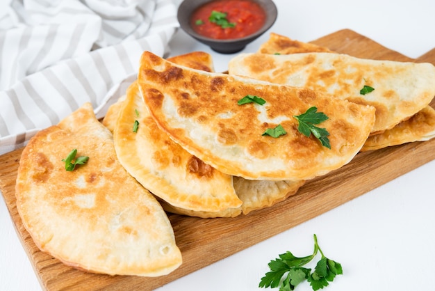 Homemade fried empanadas with pork, chebureks with mushrooms on a wooden board