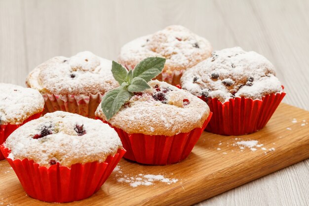 Homemade fruit muffins sprinkled with powdered sugar and fresh mint on wooden cutting board.