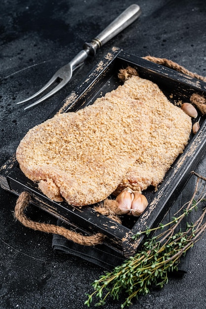 Homemade German Wiener Raw schnitzel in a wooden tray. Black background. Top view.