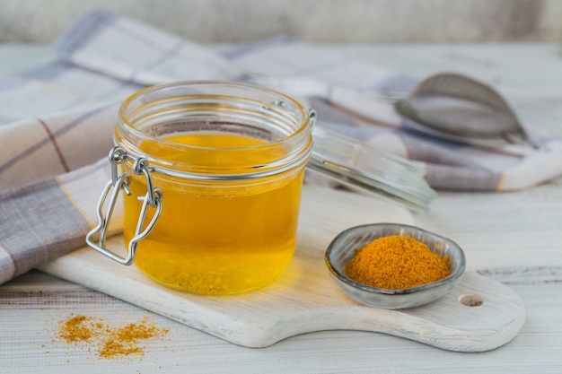 Homemade Ghee or clarified butter in a jar and turmeric on white wooden table.