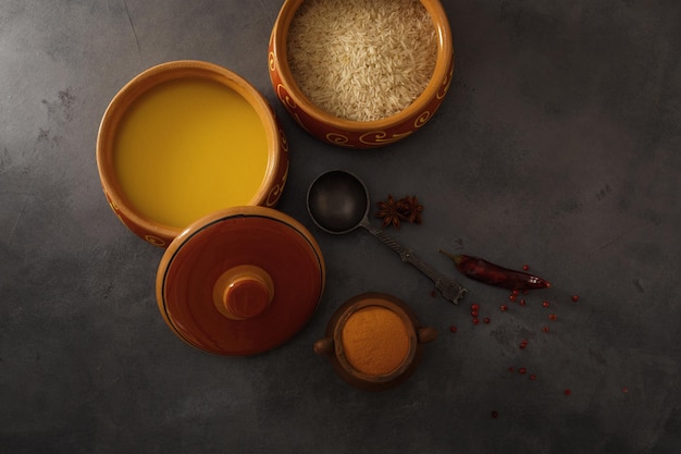 Homemade ghee, rice in a ceramic pot, red peppers and turmeric spices. Top view.