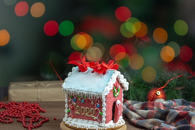 Foto casa di pan di zenzero fatta in casa sullo sfondo di un albero di natale decorato e luci sfocate