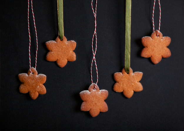 Homemade gingerbread snowflakes on ribbons on black background.