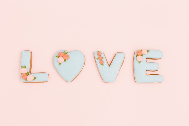 Homemade gingerbreads with letters love on background of pastel pink. Saint Valentine day composition or greeting card with copy space for text or congratulations. Minimal style.