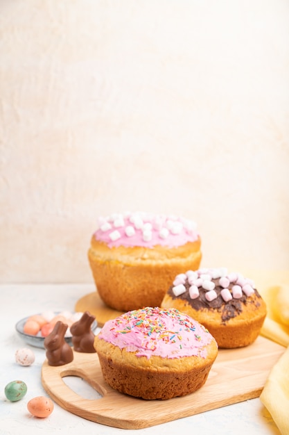 Homemade glazed and decorated easter pies with chocolate eggs and rabbits on a white concrete background. Side view, copy space, selective focus.