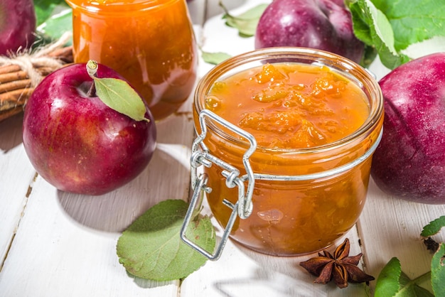 Homemade golden colored apple jam with farm red apples and leaves on white wooden background copy space