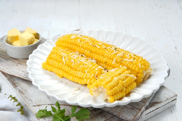 Homemade golden sweet corn cob with butter and cheese on white table