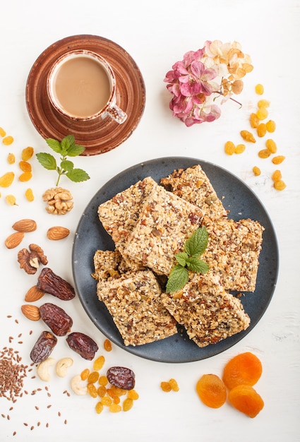 Homemade granola from oat flakes, dates, dried apricots, raisins, nuts in blue ceramic plate on a white wooden background