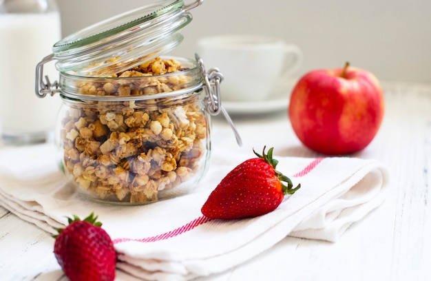 Homemade granola in a glass jar. Ingredients for a healthy breakfast - granola, apple, strawberry and milk. Close-up