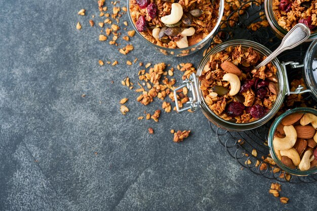 Homemade granola in glass jar with greek yogurt or milk and cashews almonds pumpkin with dried cranberry seeds in dark grey table background Healthy energy breakfast or snack Top view