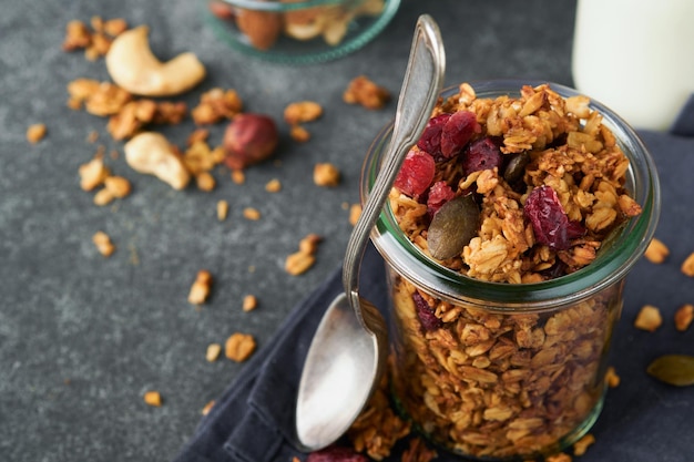Homemade granola in glass jar with greek yogurt or milk and cashews almonds pumpkin with dried cranberry seeds in dark grey table background Healthy energy breakfast or snack Top view