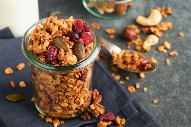 Homemade granola in glass jar with greek yogurt or milk and cashews almonds pumpkin with dried cranberry seeds in dark grey table background Healthy energy breakfast or snack Top view