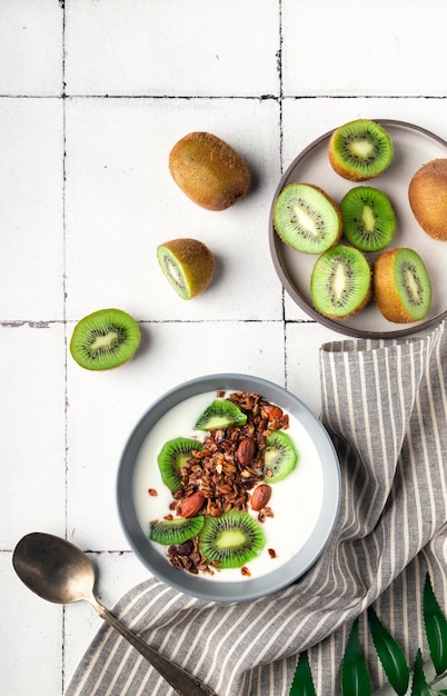 Homemade granola muesli with kiwi fruit and yogurt on white tile background Healthy breakfast bowl