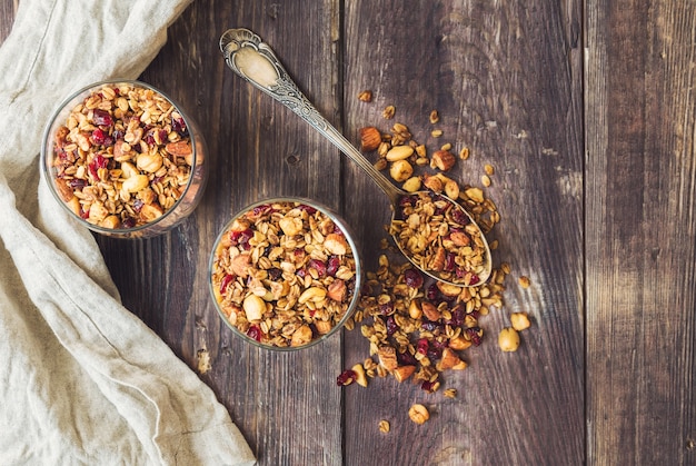 homemade granola muesli with nuts and dried cranberries in glasses on rustic wooden background