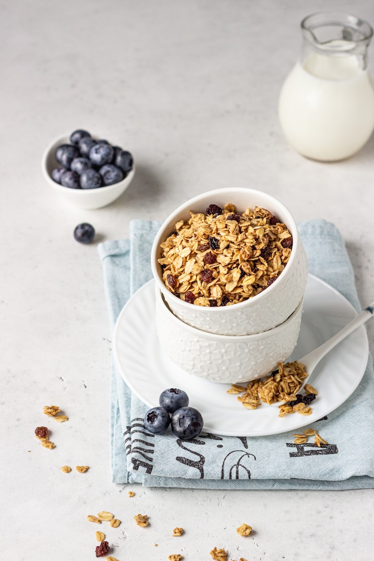 Фотография домодельный granola в белой керамической миске с изюмом, черникой и молоком. полезные ингредиенты для завтрака