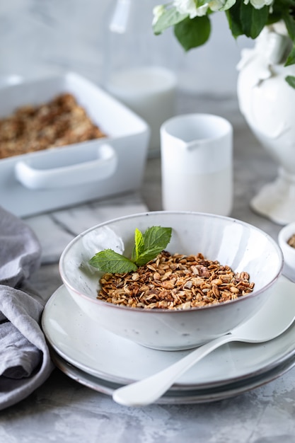 Домодельный granola в белой плите. Здоровый завтрак с мюсли, йогурт, фрукты, ягоды на белом фоне в белой тарелке.