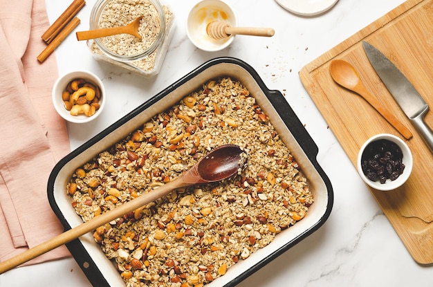 Homemade granola with nuts dried cranberries and honey in a baking pan on a white marble background