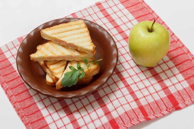 Panino al formaggio grigliato fatto in casa per colazione su un piatto e una mela sul tovagliolo