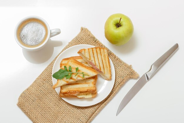 Homemade grilled cheese sandwich for breakfast on a plate and a knife a cup of coffee and an apple