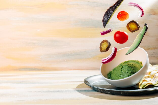 Homemade guacamole bowl with ingredients floating around it. Vintage wooden table. Healthy food