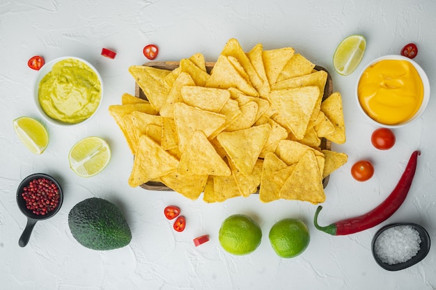 Homemade guacamole and cheese dip with nachos, on white table,\
top view or flat lay