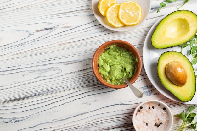 Homemade guacamole ingredients, avocado, salt, pepper, lemon and spices on wooden table