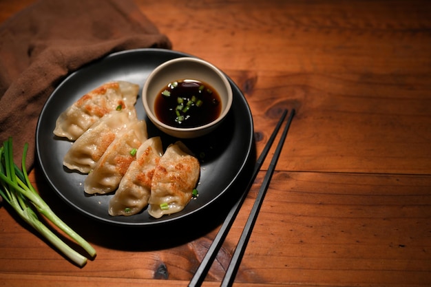 Homemade gyoza or Asian fried dumplings served with sauce and spring onion slide on wood table