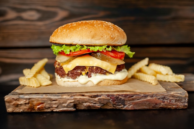 Homemade hamburger with lettuce, tomato, cheese and cucumber on a cutting board