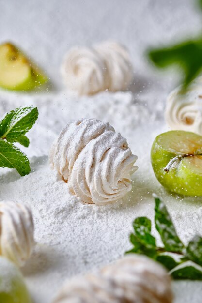 Homemade handmade apple marshmallows on a background of icing sugar. Dessert in the snow. Sweetness is decorated with apples and mint.