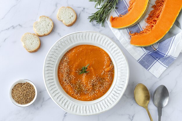 Homemade and healthy pumpkin cream with bread from above on marble table. Flat lay