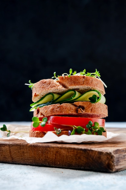 Panino sano fatto in casa con insalata di crescione di pane integrale, cetriolo, pomodoro e micro erbe su tavola di legno.