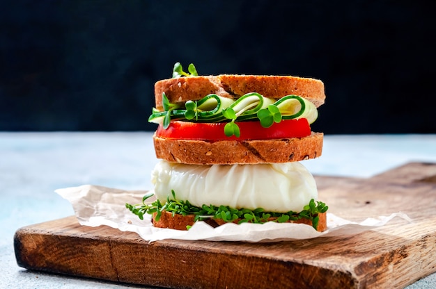 Homemade Healthy Sandwich with Wholegrain Bread, Poached Egg, Cucumber, Tomato and Micro Herbs Watercress Salad on Wooden Board.