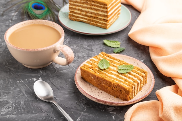 Homemade honey cake with milk cream and mint with cup of coffee on a black concrete table. Side view, close up.