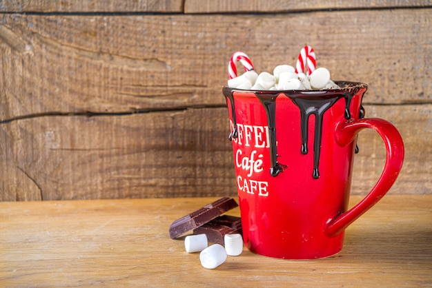 Cioccolata calda fatta in casa in tazza rossa, con mini marshmallow e gocce di cioccolato, decorazioni di bastoncini di zucchero, spazio per le copie