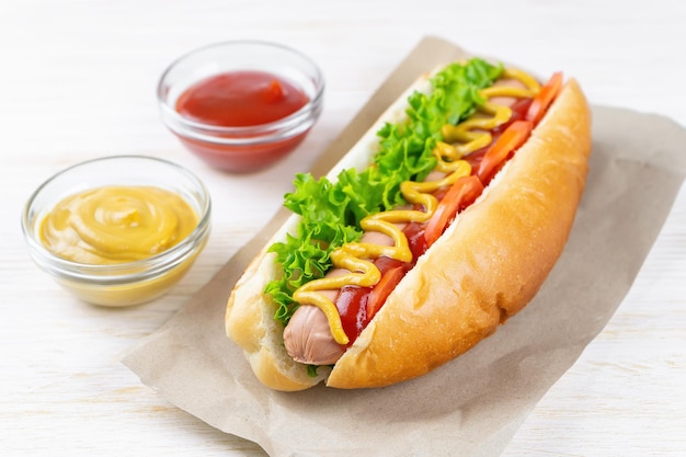 Homemade Hot Dog with yellow mustard ketchup tomato and fresh salad leaves on white wooden background Fast food street food american cuisine