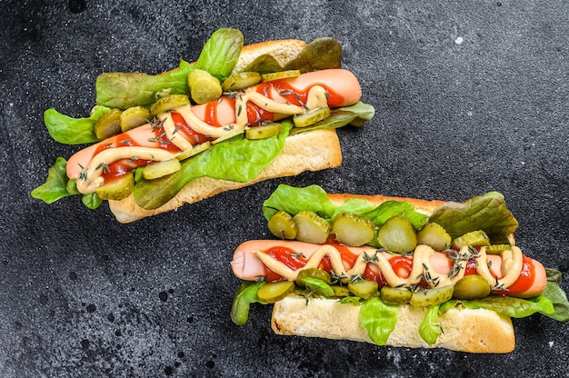 Homemade hot dogs with vegetables, lettuce and condiments. Black background. Top view.