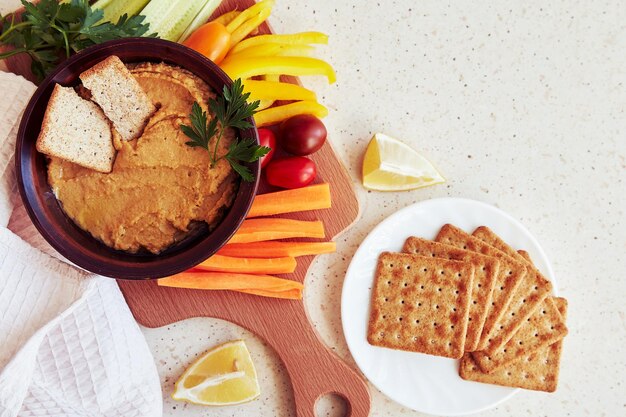 Foto hummus fatto in casa con biscotti di grano, prezzemolo, limone e verdure fresche su una tavola da taglio